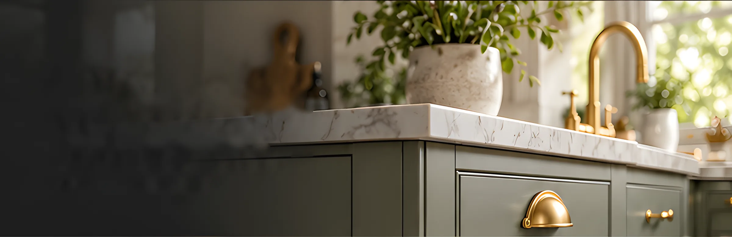 Close-up of a sage cabinet with a brass cup handle, marble worktop, plant pot and brass tap